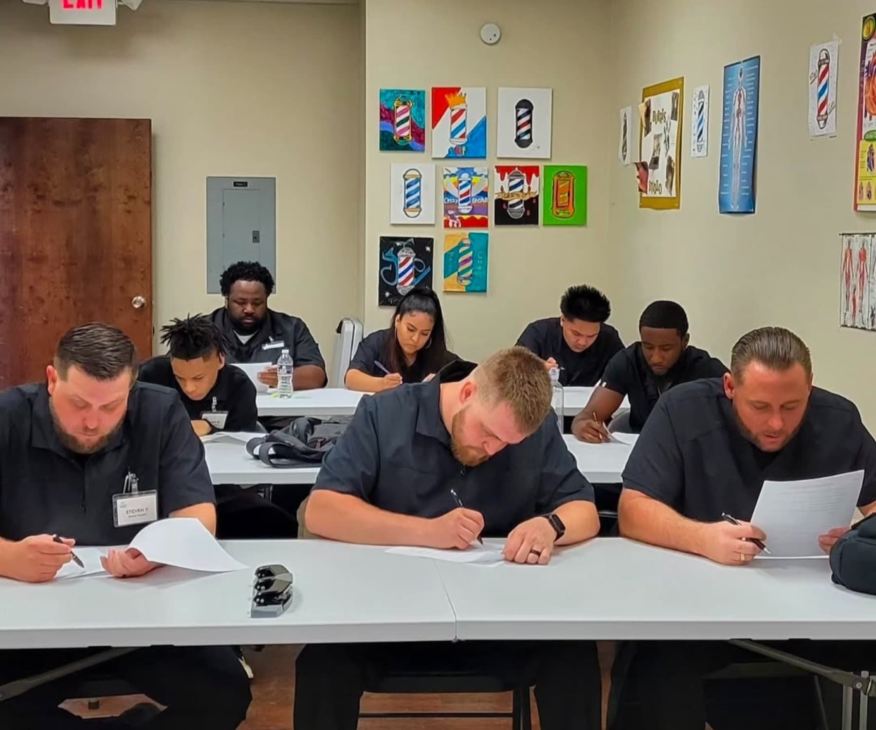 Students in matching black uniforms writing at classroom tables.